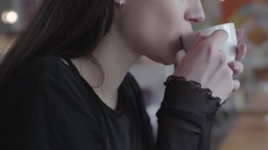 Bir kafe veya restoranda istirahat beyaz bir fincan çay veya kahve içme güzel bir genç esmer güzel kadın portre yakın. Kız bir hafta sonu veya dinlenme sahiptir. Gerçek insanlar serisi.