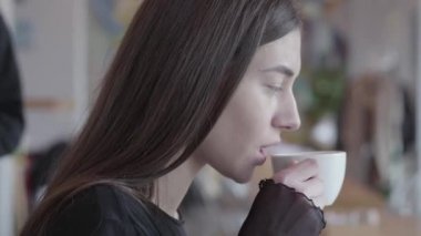 Siyah elbise beyaz fincan onun çay içme modern kafede masada oturan genç kadının yakın yukarı portre. Adamın elleri bayanın gözlerini kapıyor, kafasını açar ve gülümsüyor..