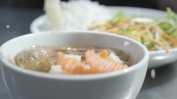 Chef puts carrot and onion in the bowl standing in front of blurred plate of noodles and vitamin salad close up. The cook prepares food for serving in restaurant. Slow motion — Stock Video