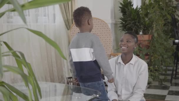 Feliz bela mulher afro-americana brincando com seu pequeno filho engraçado na acolhedora sala de estar. Relacionamento mãe e filho. Uma família feliz . — Vídeo de Stock