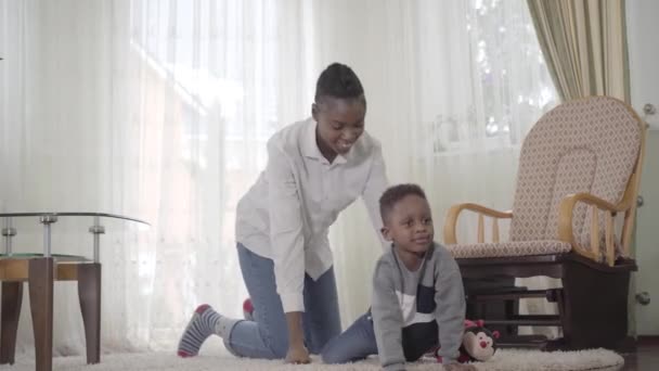 Hermosa madre afroamericana olorosa con su pequeño niño lindo divirtiéndose junto con pequeños bailes en la acogedora sala de estar. Relación madre e hijo. Una familia feliz . — Vídeos de Stock