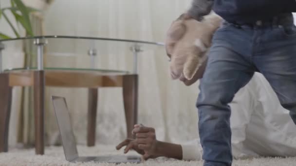 Femme d’afro-américain travaillant sur l’ordinateur portatif se trouvant sur le tapis et son petit fils mignon viennent à elle avec le jouet. Relation maman et fils. Une famille heureuse. — Video