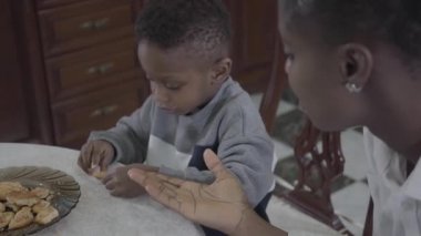 Plaka üzerinde kurabiye oynarken masa tarafından küçük oğlu ile oturan çekici Afrikalı Amerikalı kadının portresi. Aile sağlıklı kahvaltı.