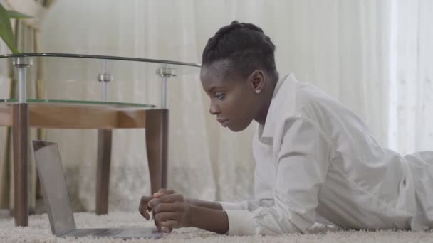 초상화 매력적인 아프리카 미국 여자 집에서 방 바닥에 바닥 매트에 누워 하루 노트북까지 그녀와 함께 작업을 집중. 프리랜서. 원격 작업. — 비디오