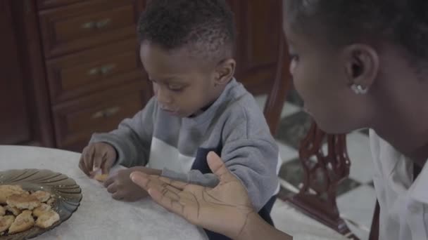 Portrét atraktivní africké americké ženy, která seděla s malým synem u stolu a hrála si sušenky na talíři. Rodina zdravá snídaně. — Stock video