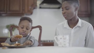 Afrikalı Amerikalı kadın küçük oğlu ile mutfakta masada oturuyor. İlişki anne ve oğul. Mutlu bir aile. Aile sağlıklı kahvaltı.