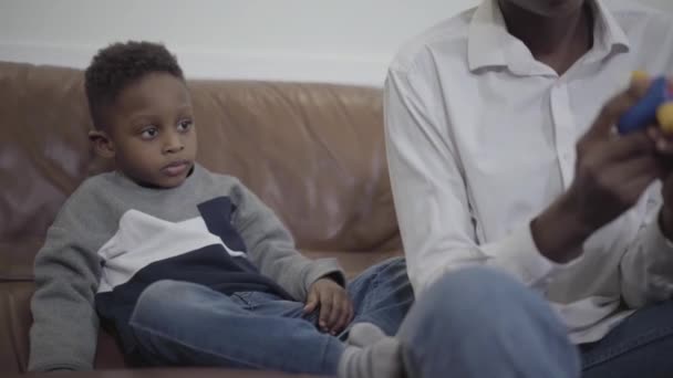 Mulher afro-americana bonito e seu pequeno filho bonito brincando com brinquedos sentados no sofá na acolhedora sala de estar. Relacionamento mãe e filho. Uma família feliz . — Vídeo de Stock