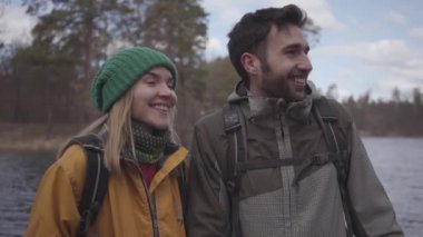 Nehir kıyısında bahar parkında bankta oturan sırt çantaları ile turistler genç çift portre güleryüzlü. Sakallı adam ve sarı ceketli güzel kadın konuşuyor ve gülüyor. Aşıklar dinlenme