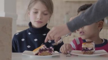 Mutlu çocuklar mutfakta masada otururken pasta yemek.