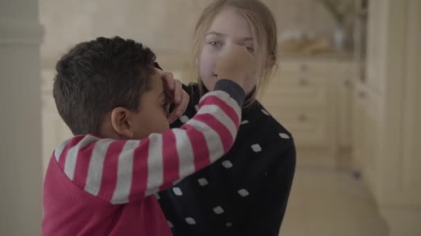 Portret van schattige Afro-Amerikaanse jongen en mooie blonde Kaukasische meisje zitten samen in de keuken. Kinderen op zoek in camera glimlachen gelukkig. Vooraanzicht, close-up — Stockvideo