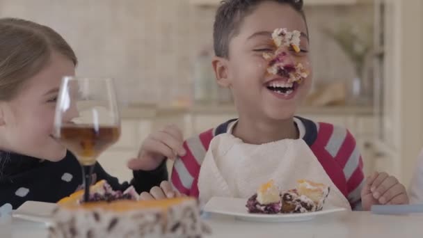 Niños felices tonteando mientras comen el pastel. Los niños se ríen. Chico afroamericano con la cara manchada en un pastel . — Vídeos de Stock