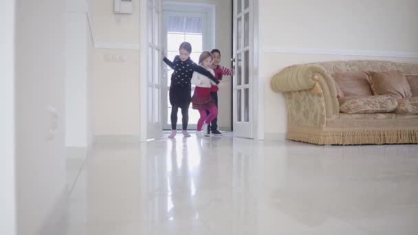 Niño afroamericano y dos chicas jugando en la casa. Tres niños felices abren la puerta y corren dentro de una gran sala de luz. Ocio de los niños en casa. Resto de niños felices. Movimiento lento . — Vídeo de stock