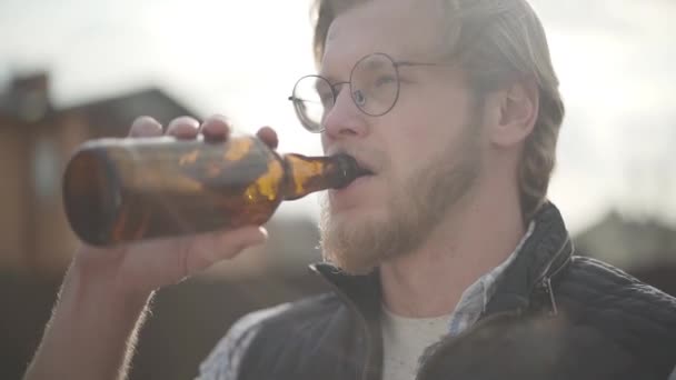 Με γένια, με γυαλιά να πίνει μπύρα και να απολαμβάνει ποτά σε εξωτερικούς χώρους. Ο τύπος έχει γεύση μπύρας από το μπουκάλι. Αργή κίνηση. — Αρχείο Βίντεο
