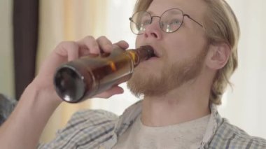 Mavi gözlü kendine güvenen sarışın adamın portresi kapalı mekanlarda bira içerek uzağa bakıyor. Gözlüklü sakallı adam kanepede evde otururken alkol içeceği zevk