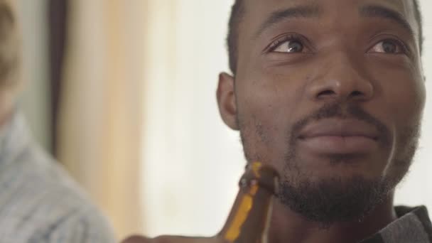 Портрет впевненого афроамериканського людини, що розмовляє і п'є пиво з друзями вдома. Дозвілля чоловіків, розслаблення. Нездоровий спосіб життя — стокове відео