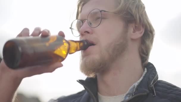 Hombre barbudo con vasos bebiendo cerveza y disfrutando de la bebida al aire libre. Chico gustos lager de botella . — Vídeo de stock
