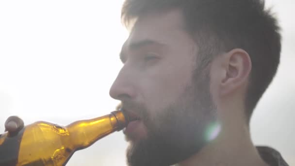 Portret aantrekkelijk bebaarde man drinken van bier en genieten van drank buitenshuis. Guy smaakt pils van fles kijkend naar de camera. — Stockvideo