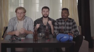 İki beyaz ve bir Afro-Amerikan erkek evde birlikte dinleniyor, tv'de boks izliyor.