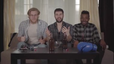 İki beyaz ve bir Afro-Amerikan erkeğin evde birlikte dinlendiği, tv'de boks seyreden portresi. Adamın bir elinde boks eldiveni var.