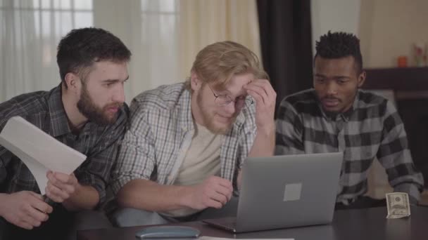 Two caucasian and one african american men resting together at home, sitting in front of laptop. Multicultural company has fun together — Stock Video