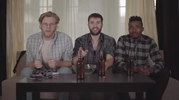 Três jovens amigos sentados em casa no cauch, olhando tv, bebendo cerveja com batatas fritas, assistindo jogo de futebol e muito desapontado e desapontado com o jogo — Vídeo de Stock