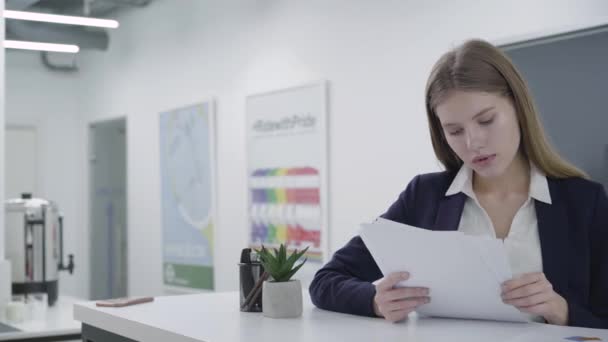 Bezorgde jonge dame in formele kleren aandachtig controleren van papieren in het kantoor staan aan de balie. Vrouw met lange haren oplossen probleem. Werkplek. Kantoorruimte. — Stockvideo