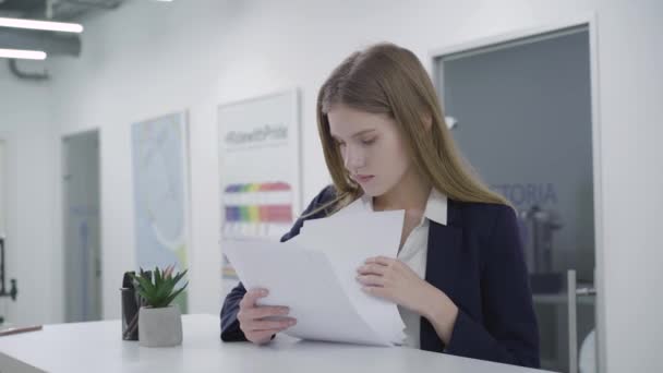 Portrait concerned thoughtful young lady in formal clothes attentively checking papers in the office standing at the counter. Woman with long hair solving problem. Working process. Camera moves left — Stock Video