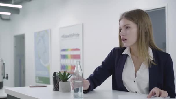 Betrokken doordachte jonge dame in formele kleren werken met papieren in het kantoor staande aan de balie. Vrouw met lang haar neemt waterfles en drankjes. Werkproces. Werkplek. Office — Stockvideo