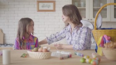 Anne ve kızı mutfakta bir sepet ve Paskalya yumurtaları ile Paskalya masasında otururken sohbet. İlişki anneleri ve kızları. Mutlu bir aile. Paskalya'nın hazırlanması.