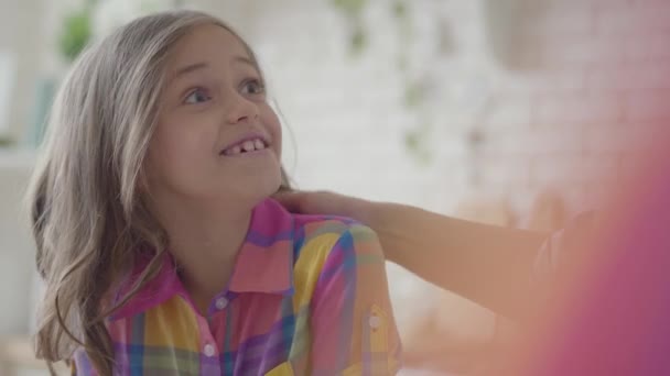 Portret van een klein schattig meisje met mooie grote ogen dragen een multicolor overhemd binnenshuis. Relatie moeders en dochters. Een gelukkige familie. — Stockvideo