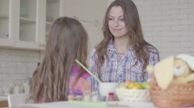 Genç anne ve tatlı kız mutfakta sohbet ediyorlar. Çocuk küçük elleriyle annenin yüzüne dokunuyor. Anne ve kızı arasında dostça bir ilişki. Mutlu bir aile..