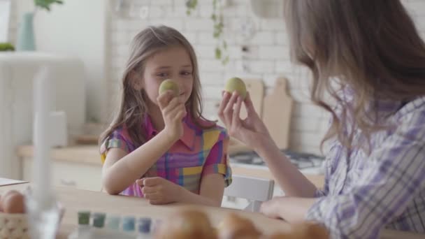 Donna e bambina che tengono le uova di Pasqua e le mostrano l'una all'altra da vicino. Preparazione per le vacanze di Pasqua. Bottiglie di vernice acrilica sul tavolo. Relazione madri e figlie. Famiglia felice . — Video Stock