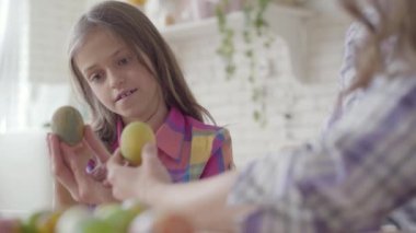 Paskalya yumurtasının üzerinde küçük bir fırçayla resim yapan kadın elini tutuyor. Paskalya tatili için hazırlık. Anne ve kızı mutfakta birlikte eğleniyorlar.