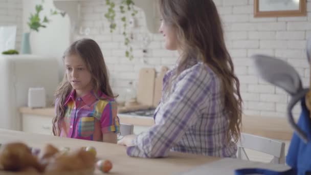 Ung mor och söt flicka sitter i köket. Flickan tar två påskägg och ger ett till mamma. Förberedelser inför påskhelgen. — Stockvideo