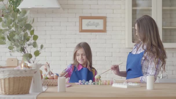 Kleines Mädchen bemalt mit ihrer Mutter Eier mit einem kleinen Pinsel. eine glückliche Familie. Vorbereitung auf das Osterfest. — Stockvideo