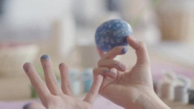 Küçük kız beceriksizce küçük bir fırça kullanarak üzerinde boyama yaparken paskalya yumurtası tutan kadın el yakın. Paskalya tatili için hazırlık. Anne ve kızı birlikte eğlenirler. Kamera sağa doğru hareket eder