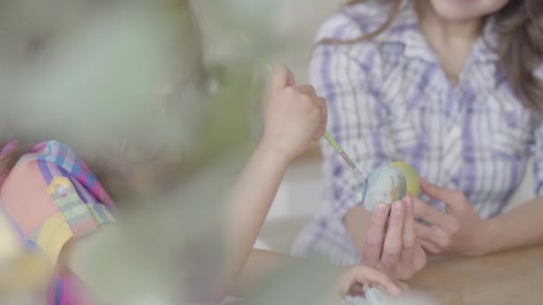Vrolijke moeder en dochter zittend aan de paastafel. Schattig meisje schildert een paasei met een dunne kwast. Relatie moeders en dochters. Een gelukkige familie. Voorbereiding van het Pasen. — Stockvideo