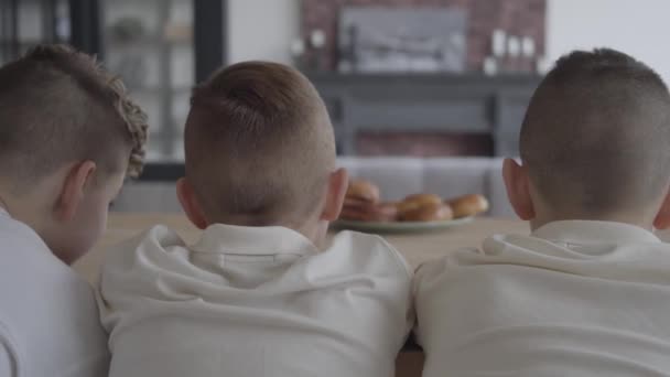 Tres chicos en primer plano mirando el plato borroso con sabrosos pasteles pequeños de pie sobre la mesa en el fondo. Los chicos tienen hambre. Concepto de alimentación — Vídeos de Stock