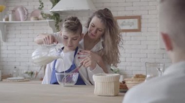 Güzel kadın ve onun genç oğlu mutfakta yemek, çocuk yemek yapmak için anne yardımcı olur. Annem kaseye süt döküp karıştırıyor, çocuğa öğretiyor. Ön planda izleyen ikinci oğul