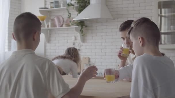 Mamma bakade bullar eller kex för sina söner. Familj med frukost vid bordet i köket. Brödraskapet. Familjerelation. — Stockvideo