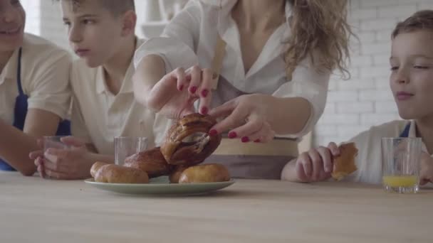 Mor och hennes fyra tonårsson äter pajer och dricker apelsinjuice i kitcken stående vid bordet närbild. Brödraskapet. Familjerelation. — Stockvideo