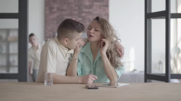 Les fils embrassent maman fatiguée debout à la table à l'intérieur. Fraternité. Relations familiales . — Video