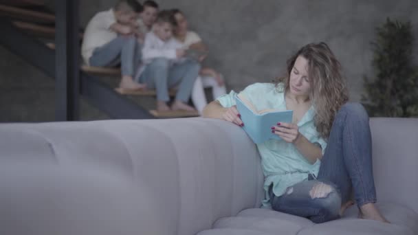 Mooie moeder het lezen van een boek aan haar zonen terwijl zittend op de Bank. Vier schattige kleine broers zitten op de trap binnenshuis. — Stockvideo