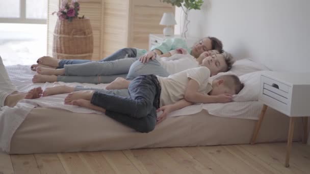 Retrato joven madre con sus hijos adolescentes durmiendo juntos en la cama grande. Un chico sentado en la silla. Feliz concepto de familia amorosa. Hora tranquila en la familia con muchos niños — Vídeo de stock