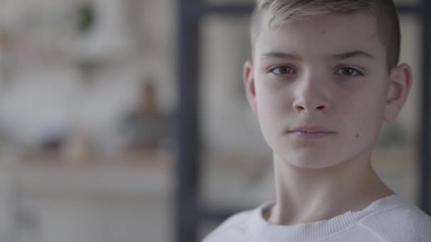 Close up portrait of a young boy looking in camera. The emotionless boy in a white t-shirt. Real people. — Stock Video