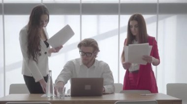 Gözlüklü sarışın adam, iş arkadaşlarının kendisine getirdiği belgeleri imzaladığı masada netbook ile hafif ve rahat bir ofiste oturuyor. Patronun her iki tarafında duran resmi giyim iki kız