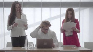 Netbook ile hafif rahat bir ofiste oturan gözlük portre sarışın adam. Patronun her iki tarafında duran kağıtları ile resmi giyim iki kız.