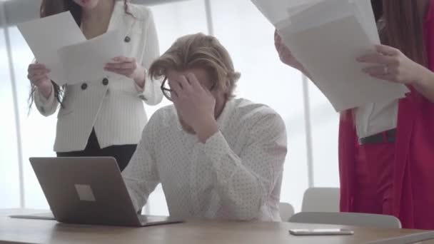 Cansado homem estressado sentado em um escritório confortável com netbook na mesa assinando documentos que colegas do sexo feminino trouxeram para ele. Duas meninas em desgaste formal em pé de cada lado do chefe — Vídeo de Stock