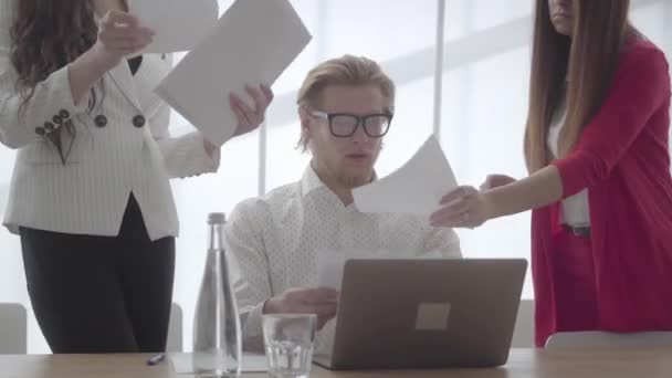 Nervös man sitter i ett bekvämt kontor med Netbook vid bordet undersöka dokument som två kvinnliga kollegor ger honom en efter en, sedan kasta papper upp. Chefen är trött och stressad — Stockvideo