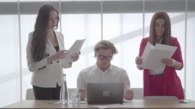 Portre sinir adam iki kadın meslektaşları ona birer birer verir belgeleri toplama masada netbook ile modern ofiste oturan, sonra kağıt yığını atmak. Patron yorgun ve.